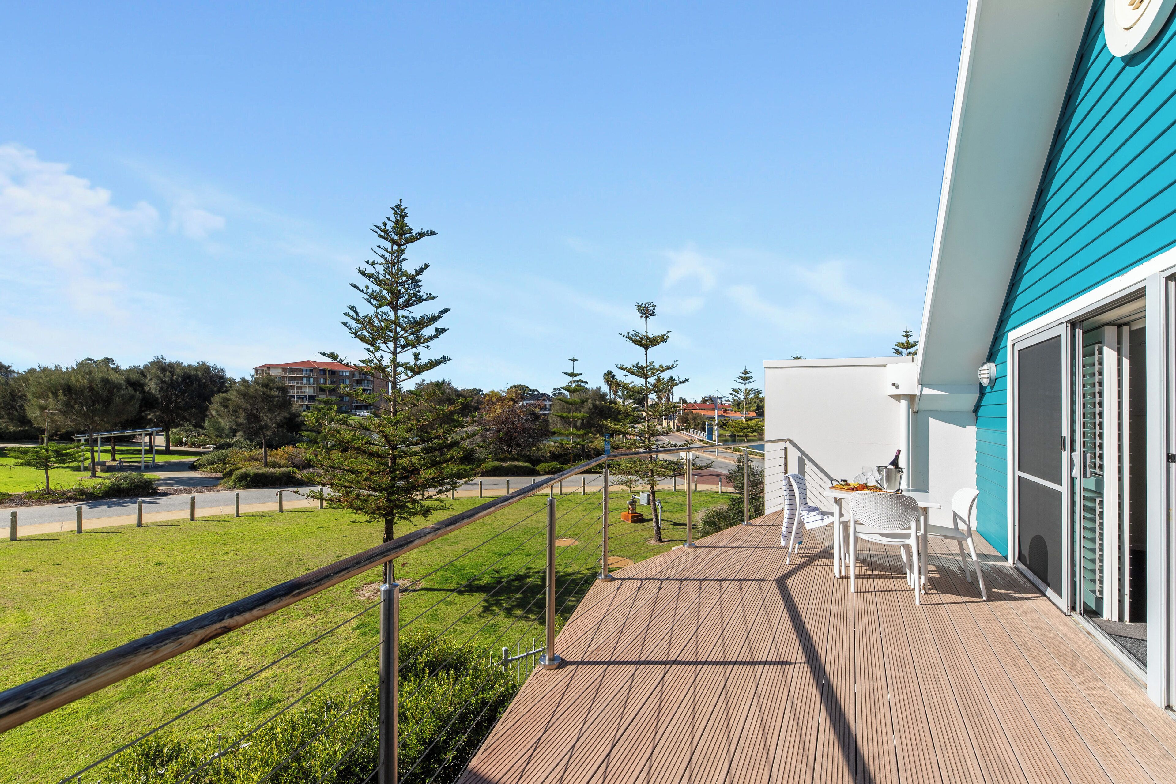 A balcony with a view of a green lawn and trees, a white building in the background, and a blue exterior wall.