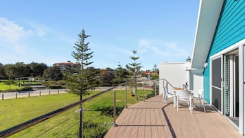 A balcony with a view of a green lawn and trees, a white building in the background, and a blue exterior wall.