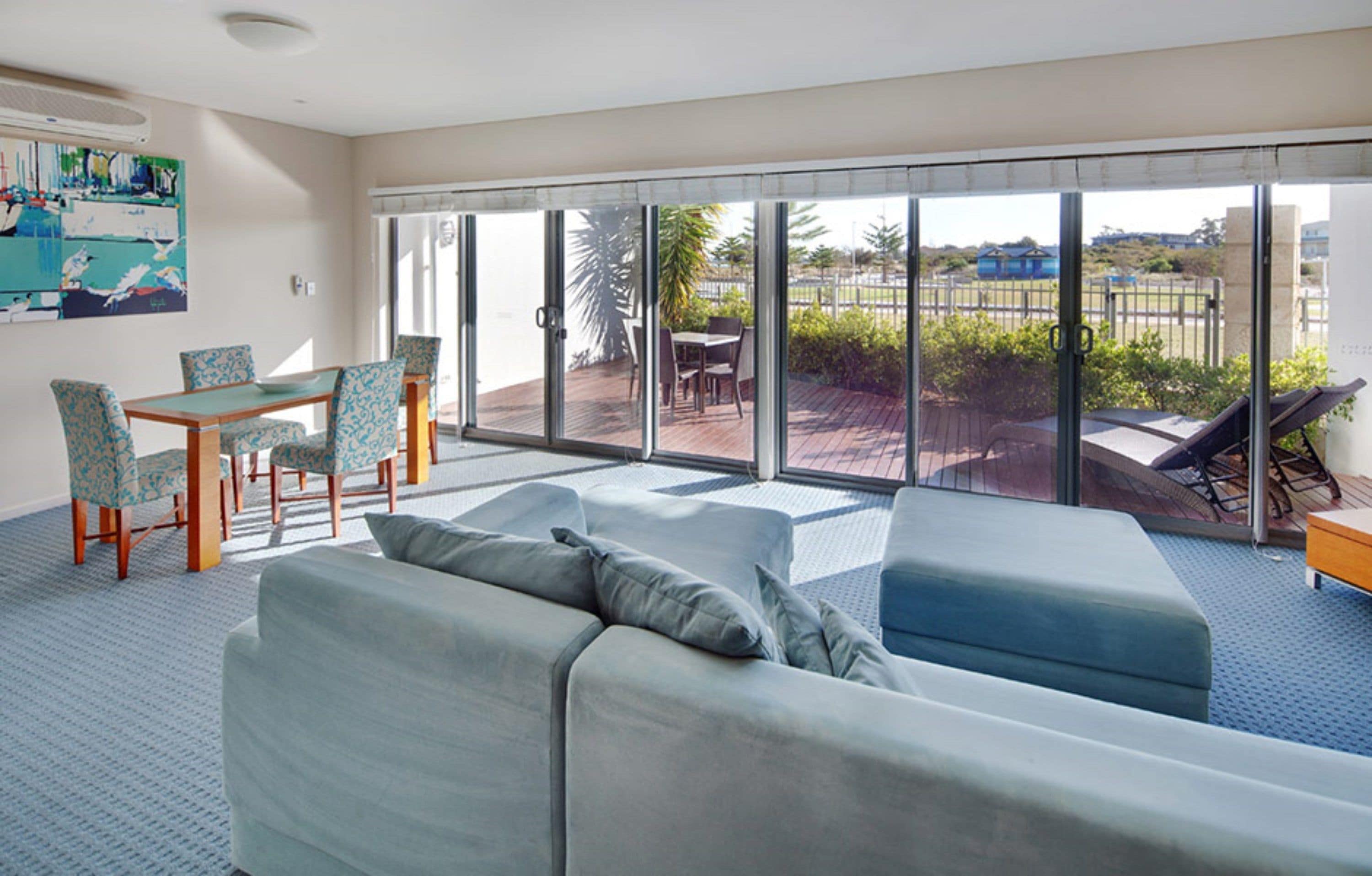 A modern living room with a sofa, chairs, and a dining table. There is a large sliding glass door leading to an outdoor patio area.