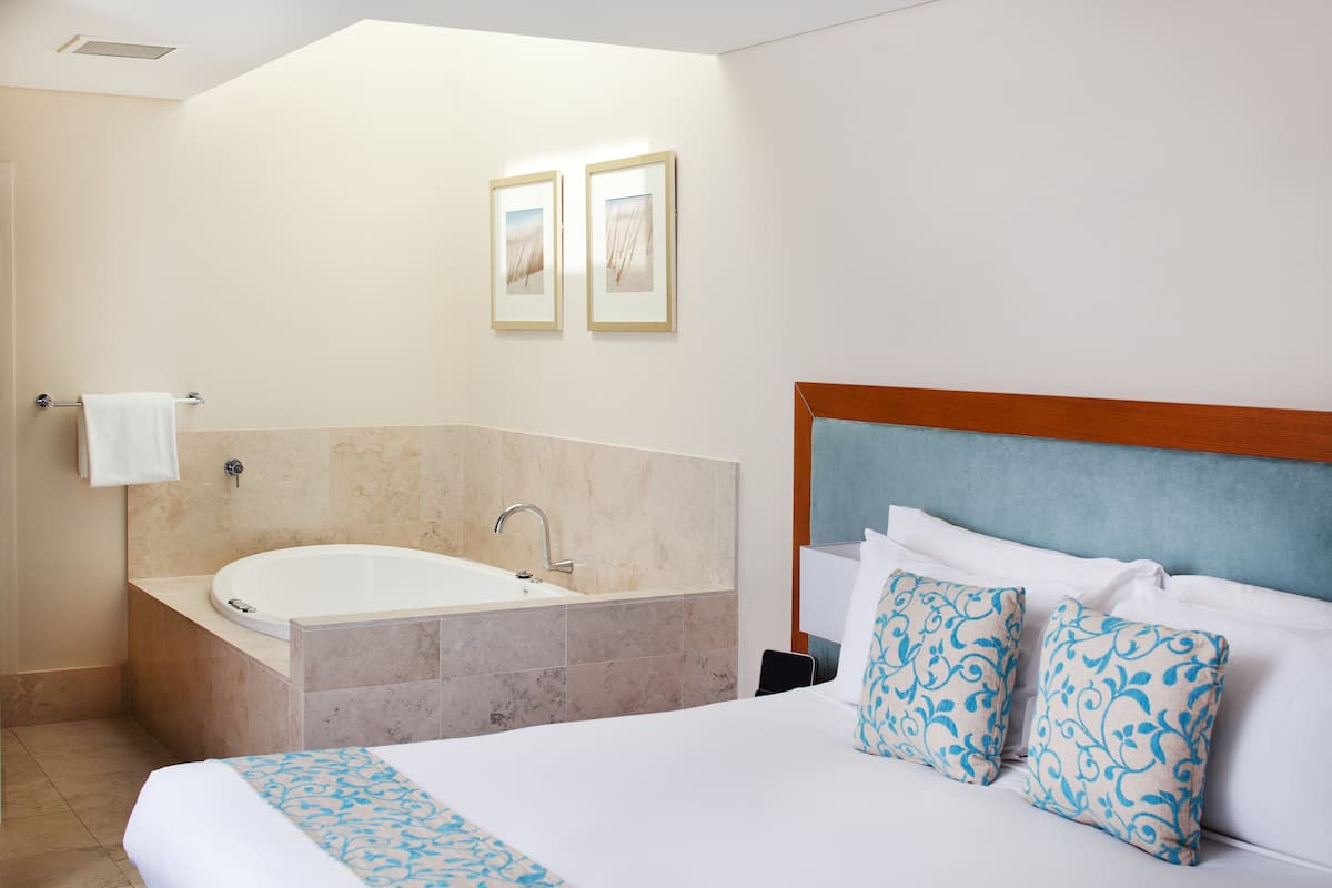 A hotel room with a large bed, a bathtub, and two framed pictures on the wall.