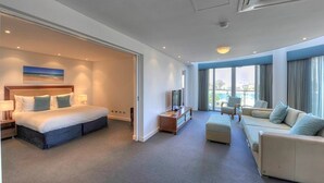 Una habitación de hotel moderna con una cama grande, un sofá, un televisor y un balcón con vistas a la ciudad.