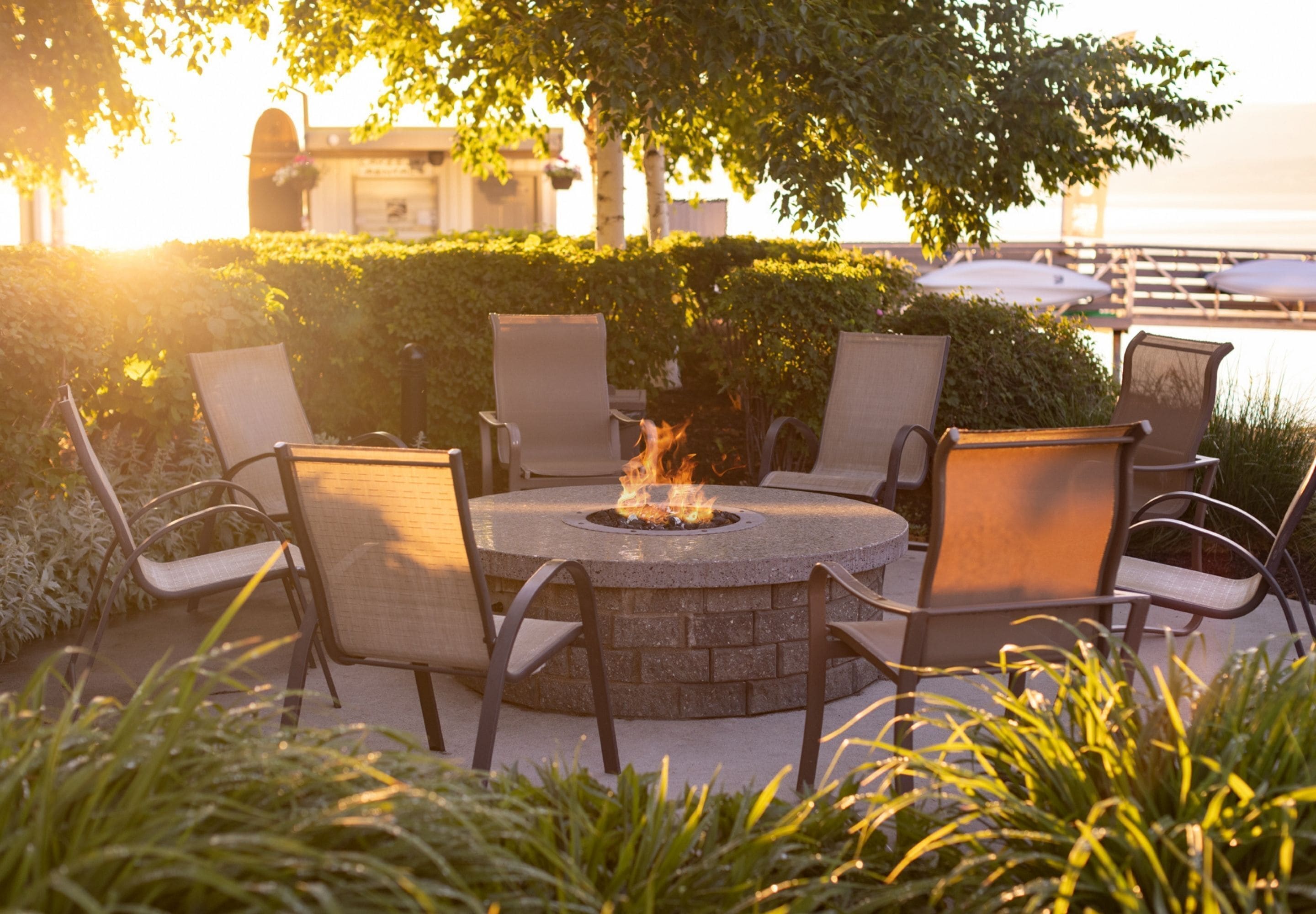 A circular outdoor seating area with a fire pit, surrounded by chairs and plants.
