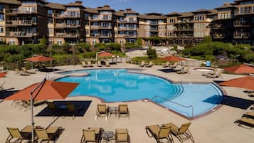 Ein Hotelpoolbereich mit mehreren Liegestühlen und Sonnenschirmen, umgeben von mehrstöckigen Gebäuden mit Balkonen.