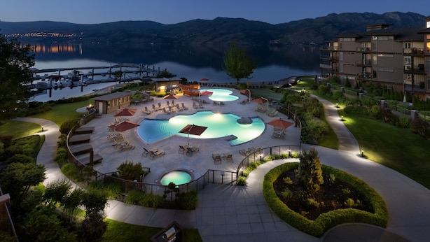 Een resort met meerdere zwembaden, buitenterras en uitzicht op een meer en bergen.
