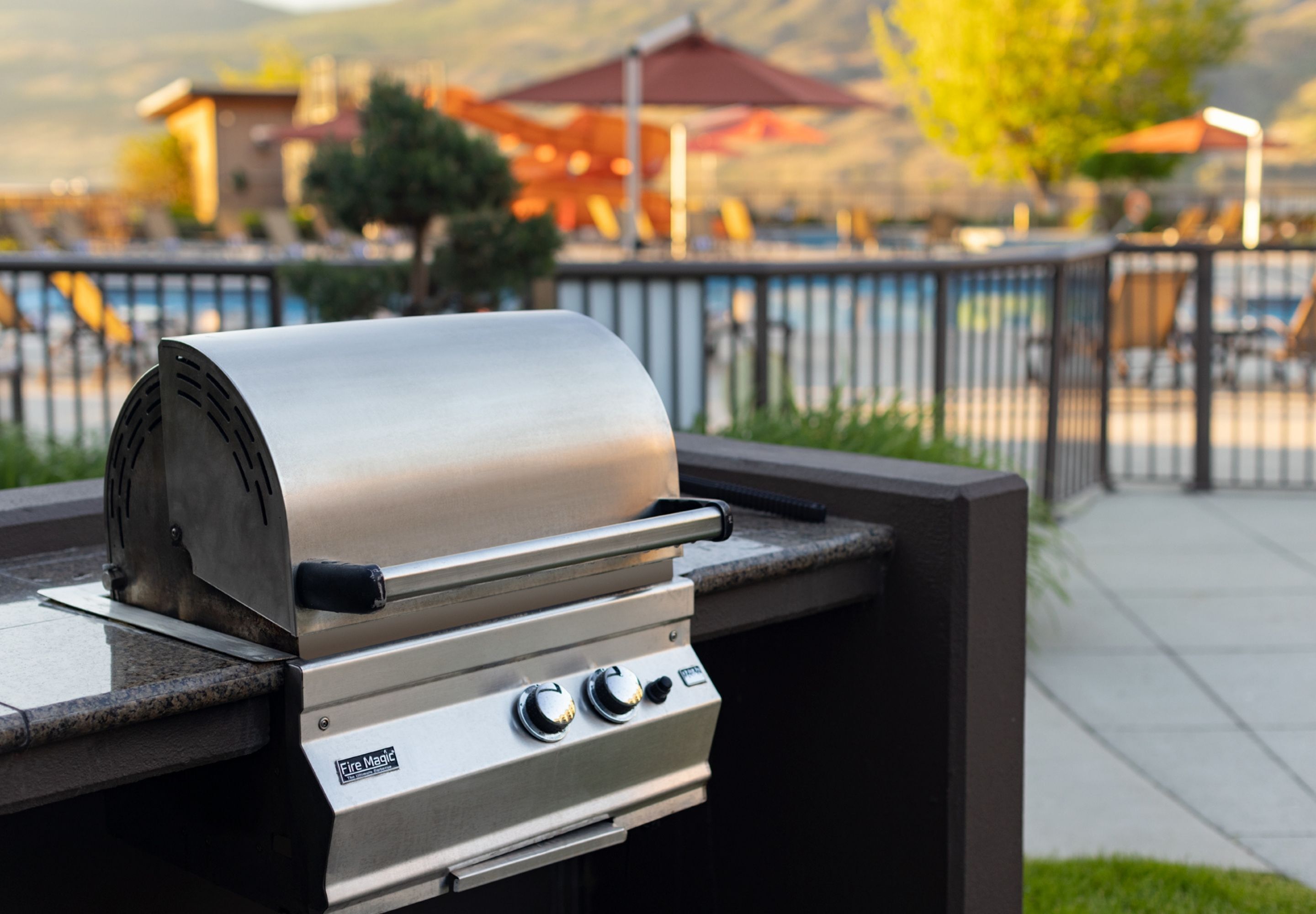 Ein Grill aus Edelstahl mit digitaler Anzeige, platziert auf einer Terrasse mit Blick auf ein Schwimmbad und Berge im Hintergrund.