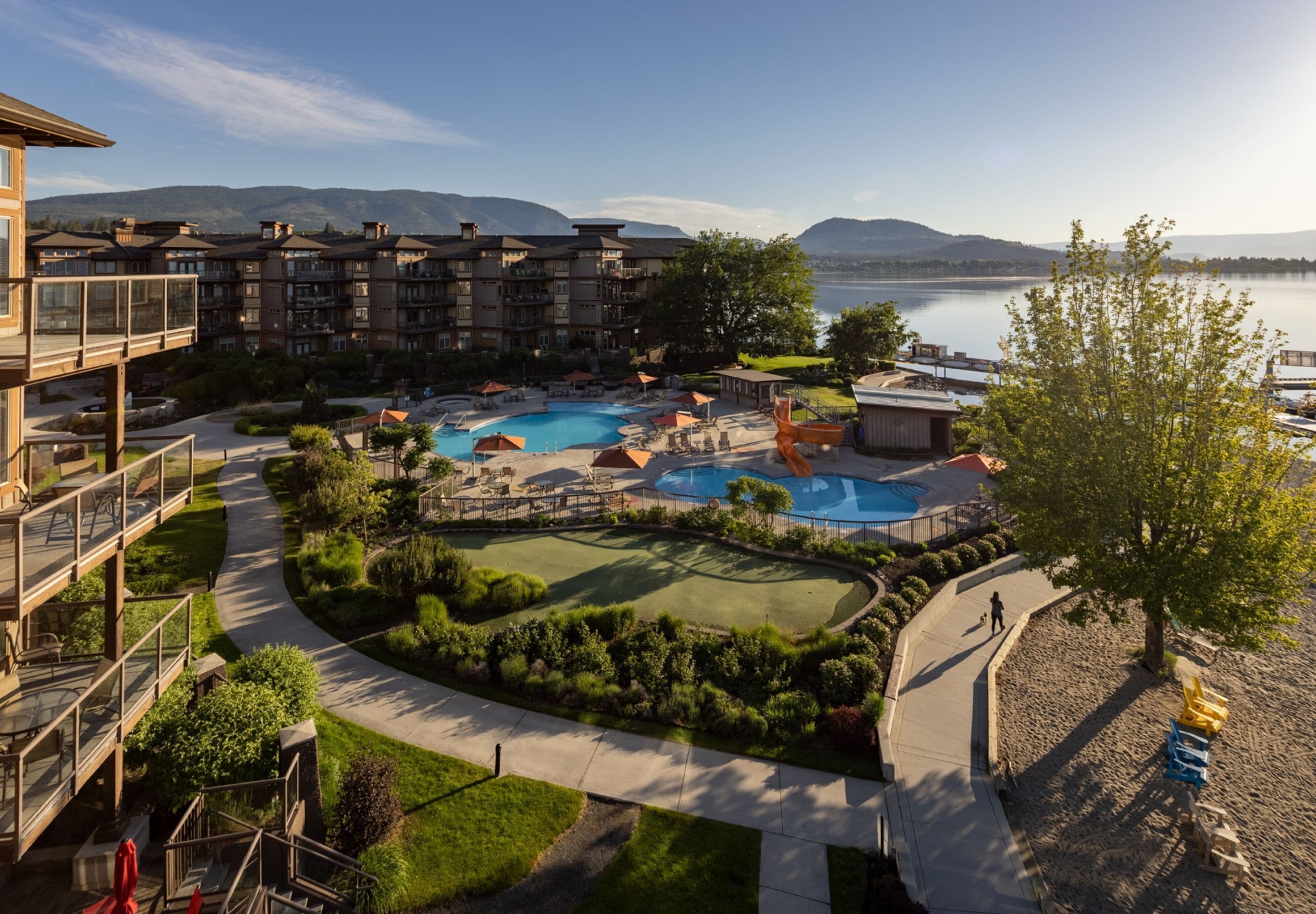 A resort with multiple swimming pools, a golf course, and a view of mountains and a lake.