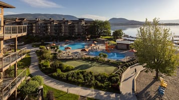 A resort with multiple swimming pools, a golf course, and a view of mountains and a lake.