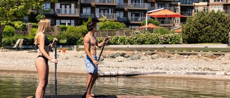 Two people on paddleboards in a calm water body with a residential building in the background.