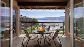 Een balkon met een tafel voor twee, uitkijkend op een meer en een bergachtig landschap.