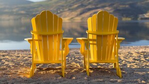 Twee gele Adirondack-stoelen kijken uit op een rustig meer met bergen op de achtergrond.