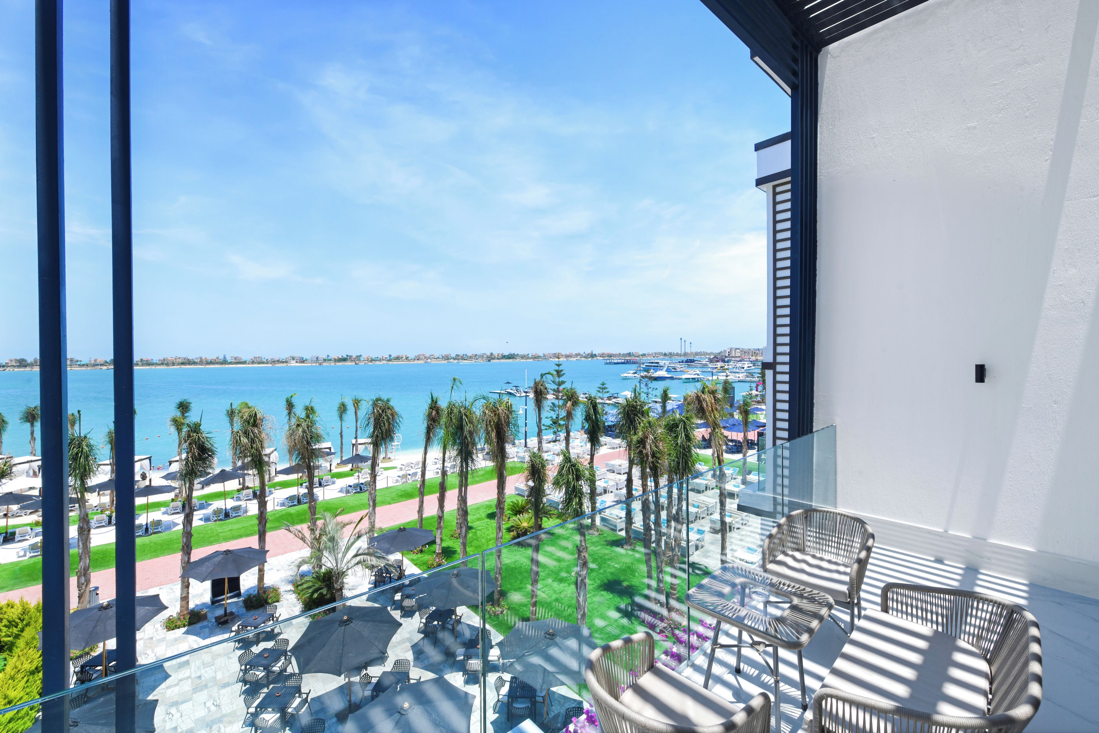 A balcony with outdoor furniture, a view of the beach, and palm trees.