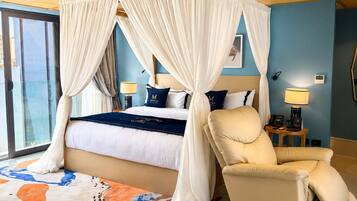 Habitación de hotel con cama con dosel, sillón, ventana grande y alfombra estampada.
