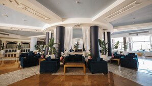 Un hall d’entrée spacieux avec un espace salon central, de grandes colonnes et un plafond haut.