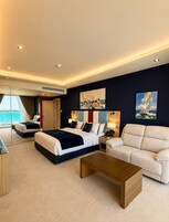 Habitación de hotel moderna con una cama grande, un sofá, una mesa de centro y vistas al mar.
