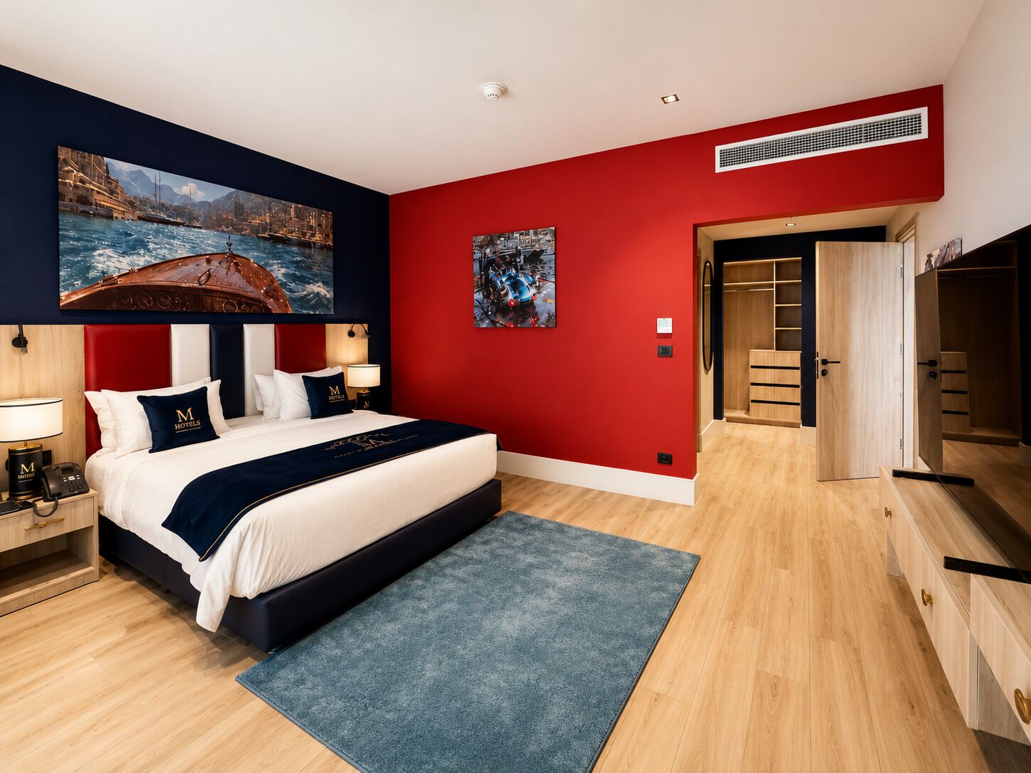 A modern hotel room with a large bed, a red accent wall, and artwork.