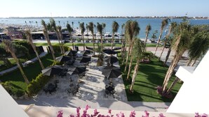 Un espace extérieur aménagé en terrasse, avec des tables et des parasols, des palmiers et une vue sur l’eau.