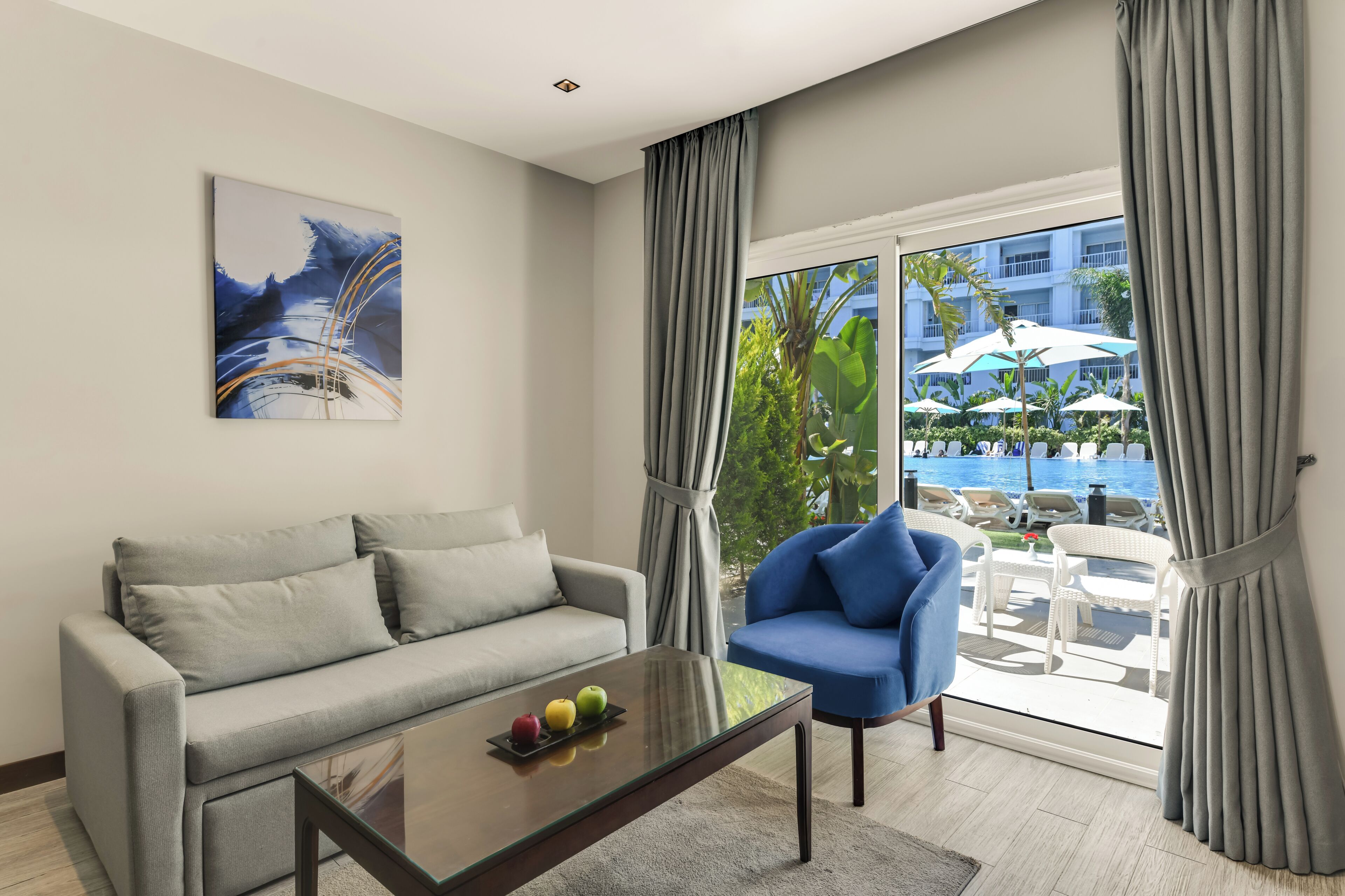 A modern living room with a grey sofa, a blue armchair, and a glass coffee table with fruit.