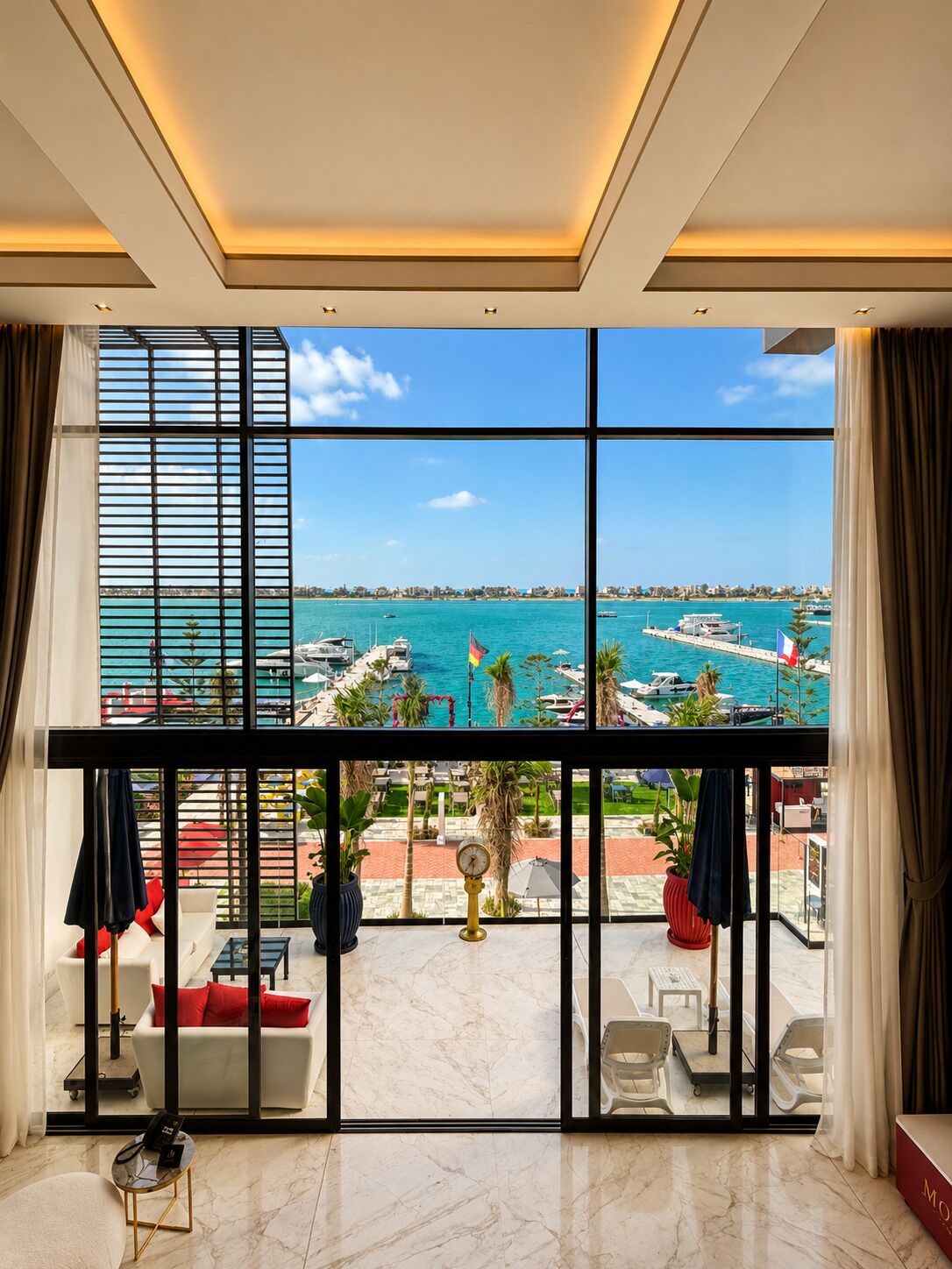 A room with a large window overlooking a marina with boats and a clear blue sky.