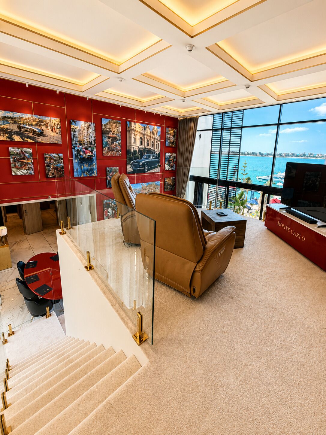 A spacious living area with a large window, a leather sofa, a red reception desk, and a staircase leading to an upper level.
