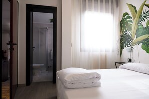 A hotel room with a bed, a bathroom with a toilet and shower, and a large window with curtains.