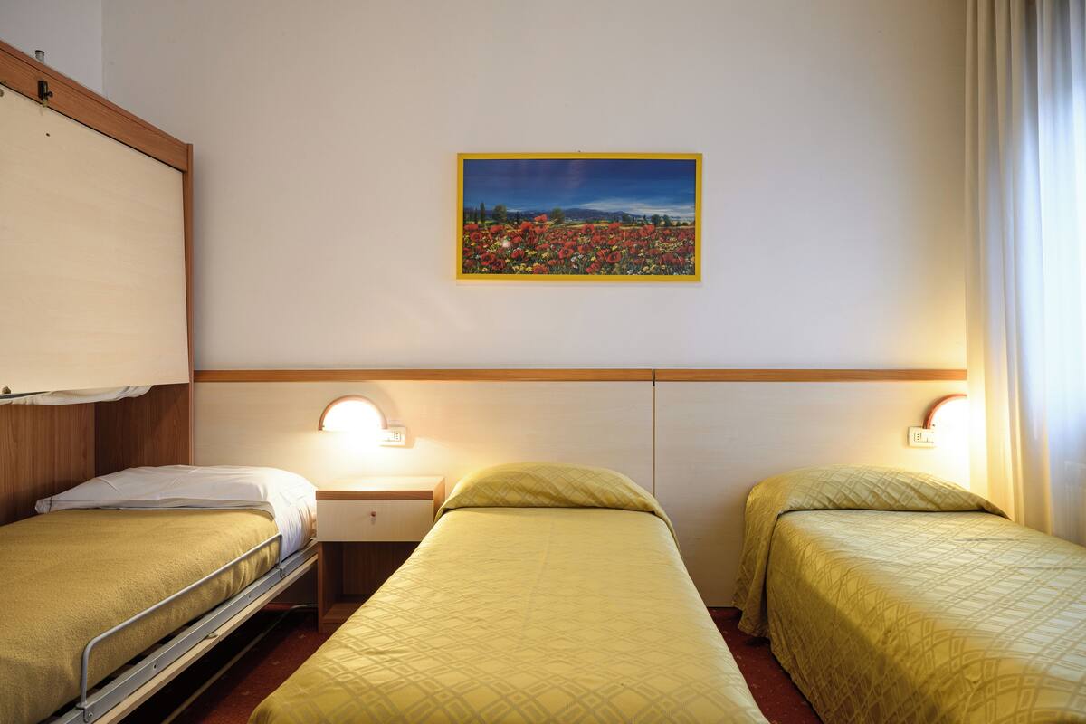 A hotel room with two single beds, a bedside table with a lamp, and a wall-mounted painting.