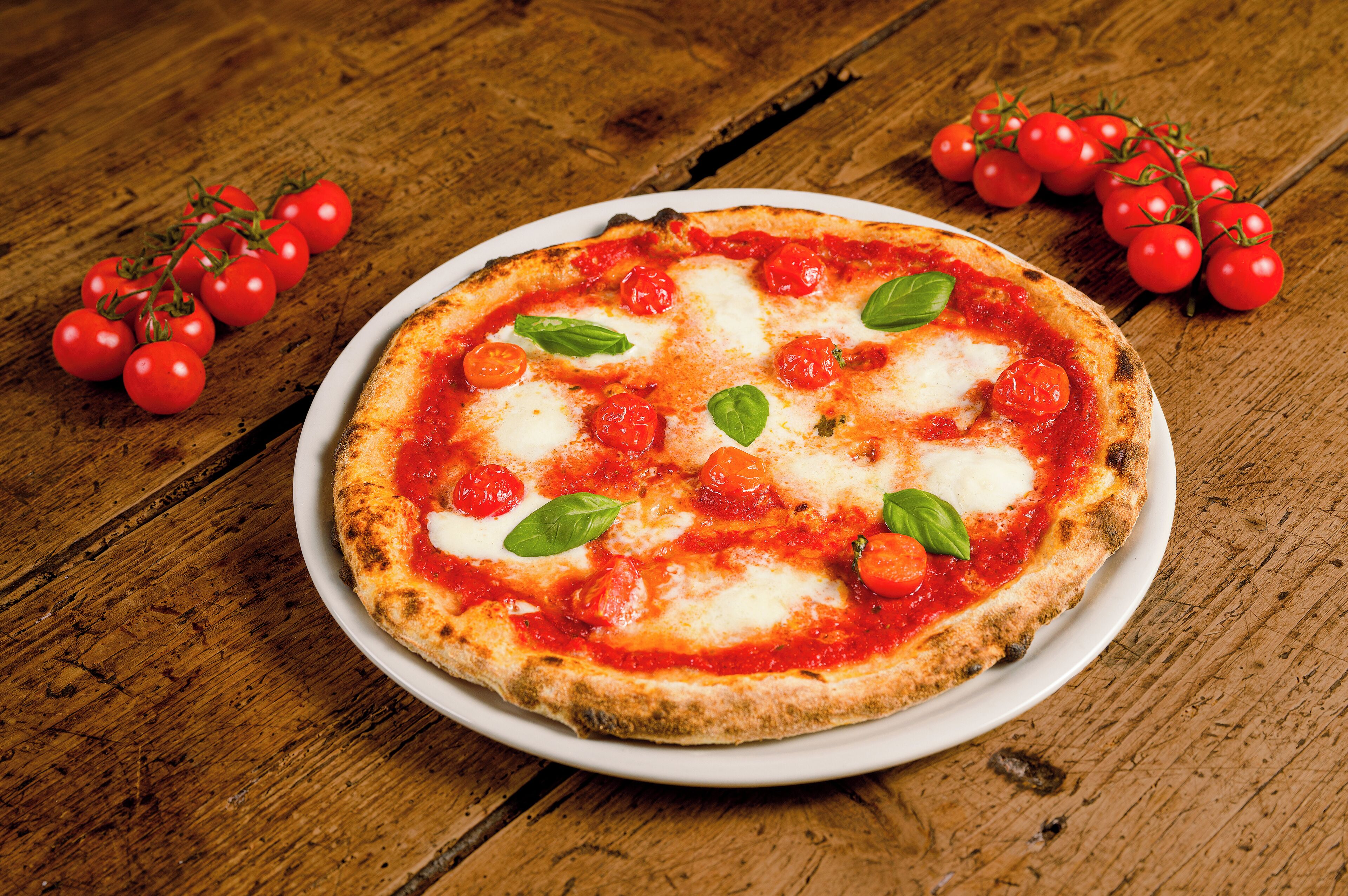 A pizza on a white plate with tomato sauce, cheese, and basil leaves, placed on a wooden table.