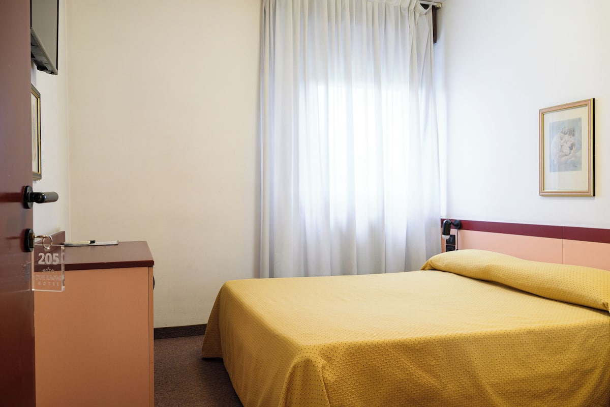 A hotel room with a bed, a desk, and a window with curtains.