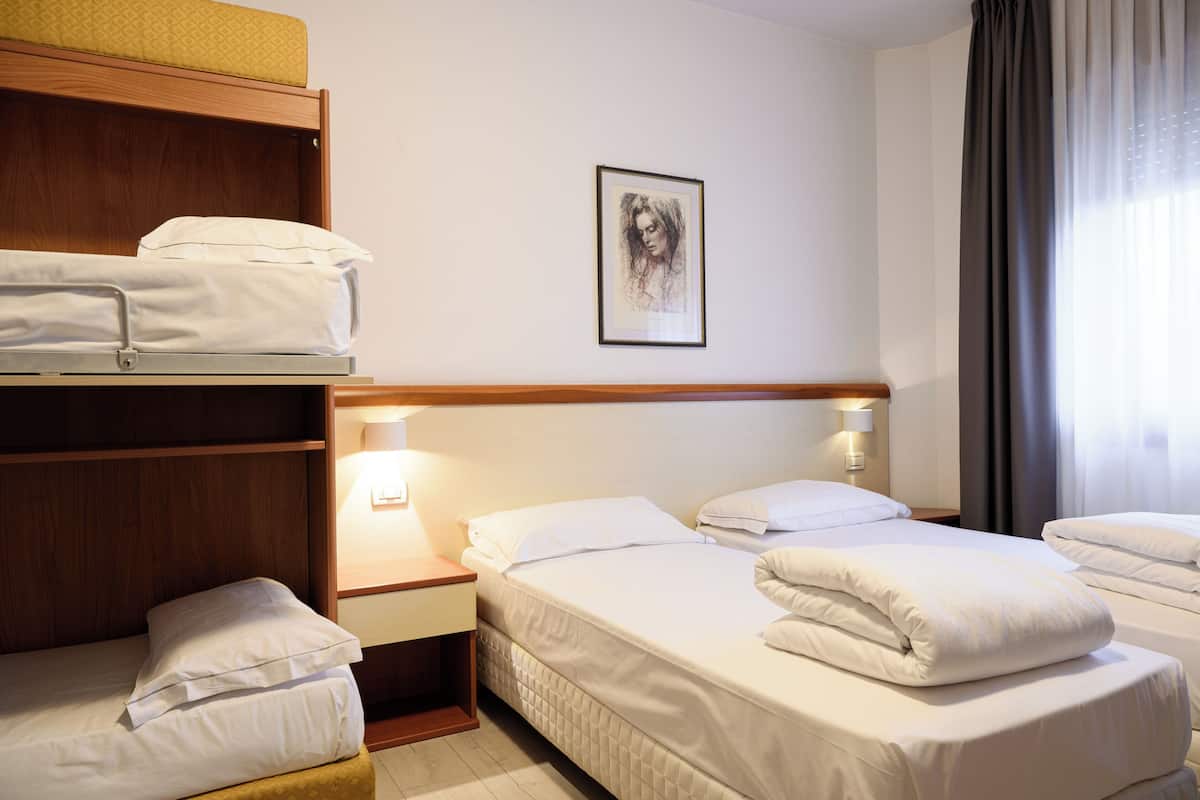 A hotel room with two beds, a bunk bed, a framed artwork on the wall, and a window with curtains.