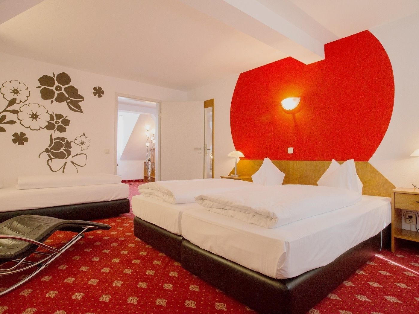 A hotel room with a large bed, a red wall decoration, and a patterned carpet.