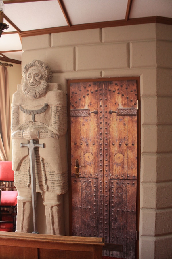 A stone statue of a figure holding a sword in front of a wooden door with metal reinforcements.