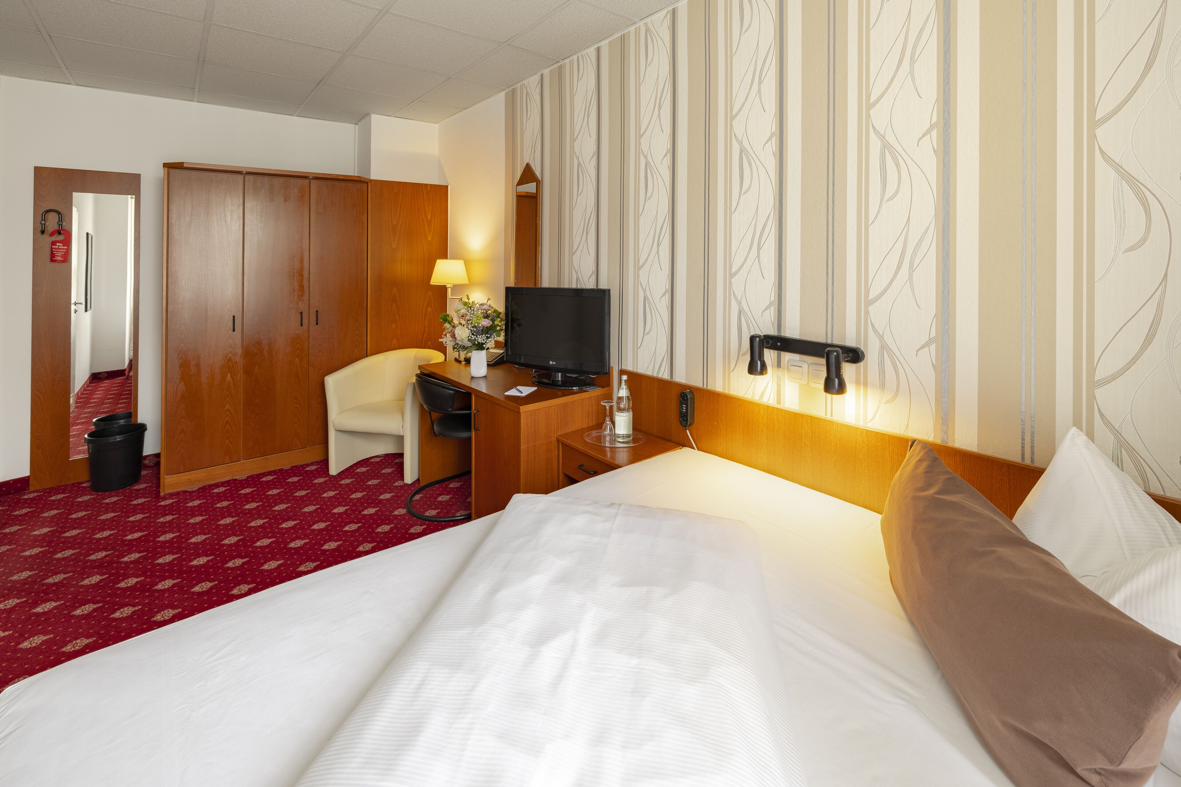 Una habitación de hotel con una cama, un escritorio con televisor, una silla y un armario.