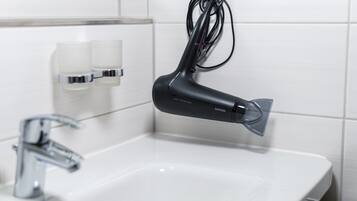 Un baño moderno con un lavamanos blanco, un grifo cromado y un secador de pelo negro montado en la pared.