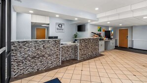 A reception area with a modern design, featuring a reception desk, a mounted television, and a sign that reads "Quality by Choice Hotels."