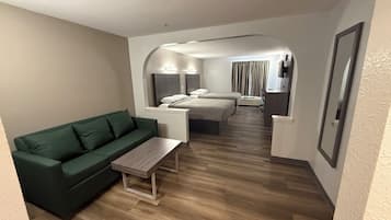 Ett modernt hotellrum med en grön soffa, ett soffbord i trä, en säng med en sänggavel och en tv som är monterad på väggen.