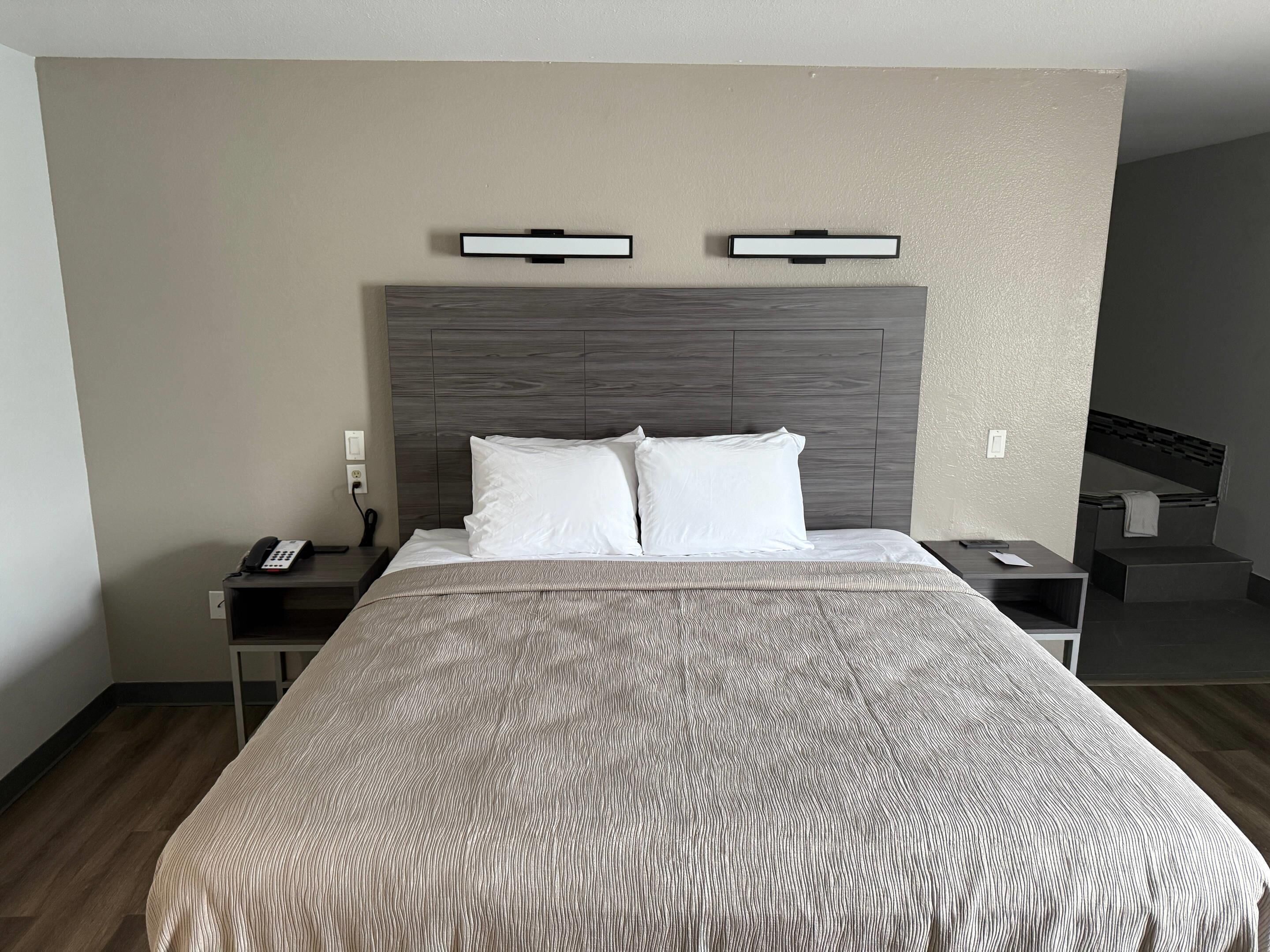 A hotel room with a large bed, two bedside tables, a telephone, and a headboard with built-in lighting.