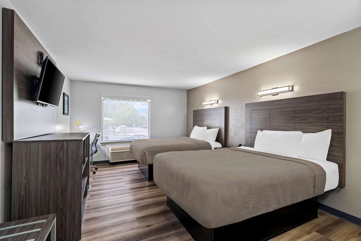 A hotel room with two beds, a desk, a TV, and a window with a view.