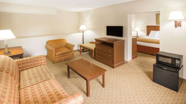 Habitación de hotel con sofá, mesa de centro, televisor, escritorio con lámpara, cama y microondas.