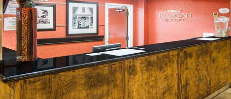 A reception desk with a wooden panel design, a framed welcome sign, and a logo for Baymont Inns & Suites.