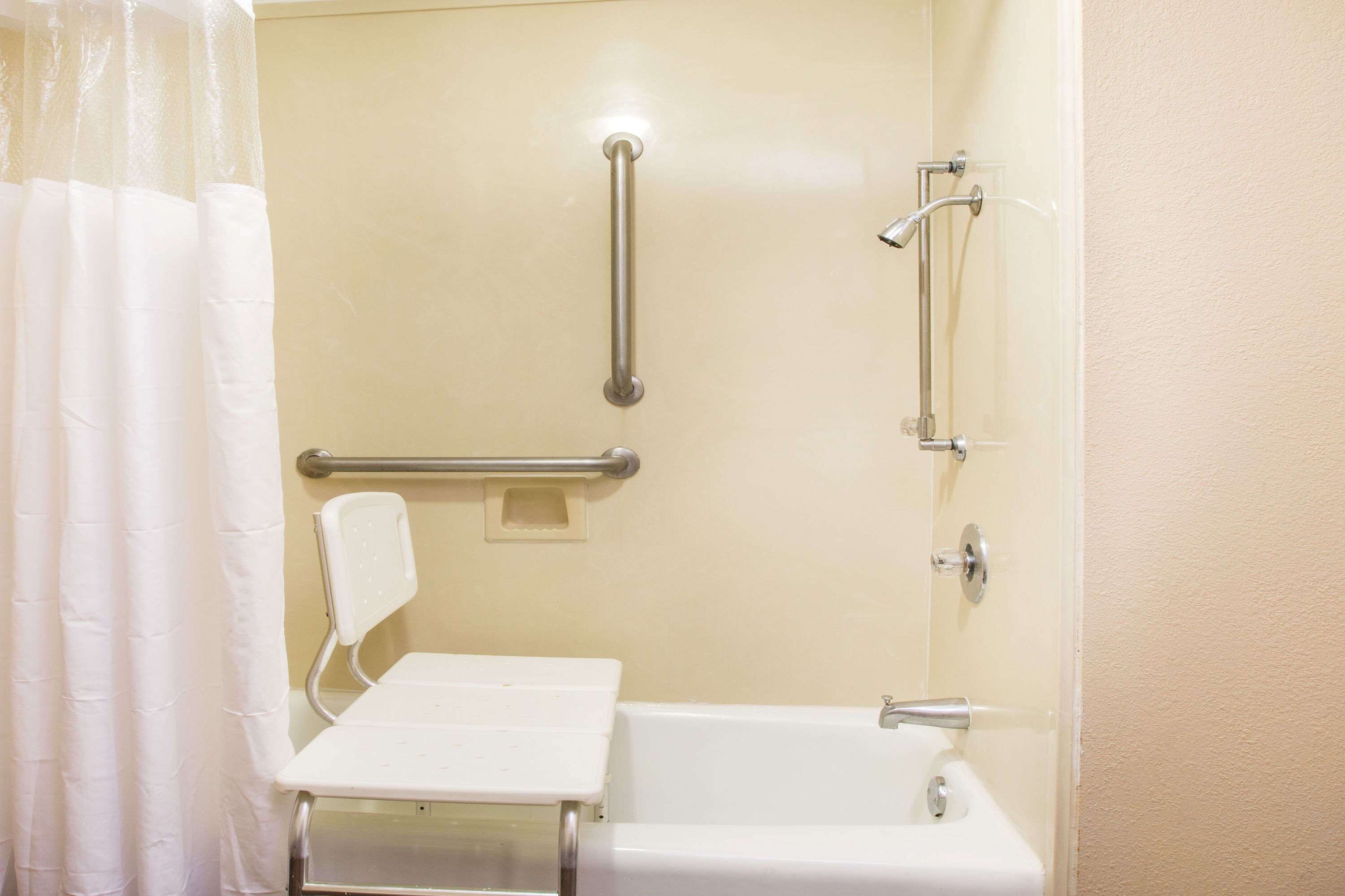 Une salle de bain avec une baignoire blanche, une douche équipée d’un pommeau de douche amovible et d’une barre d’appui.