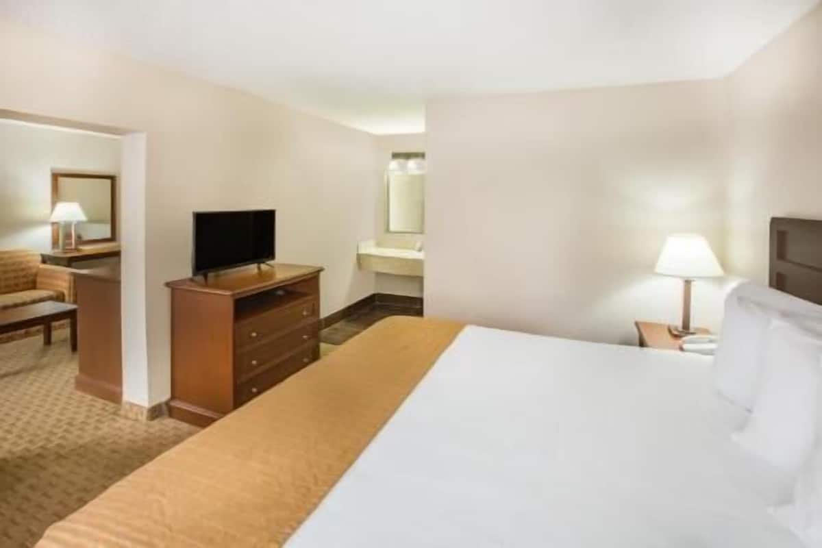 A hotel room with a bed, a TV, a desk with a lamp, and a bathroom.