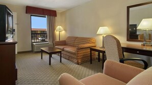 Habitación de hotel con sofá, sillón, escritorio y un amplio ventanal con vista a un edificio.