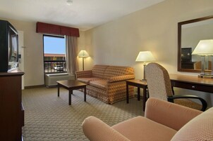 Habitación de hotel con sofá, sillón, escritorio y un amplio ventanal con vista a un edificio.