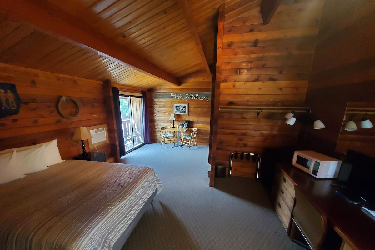 Habitación de cabaña de madera con una cama, un escritorio, una silla y una mesa de comedor.
