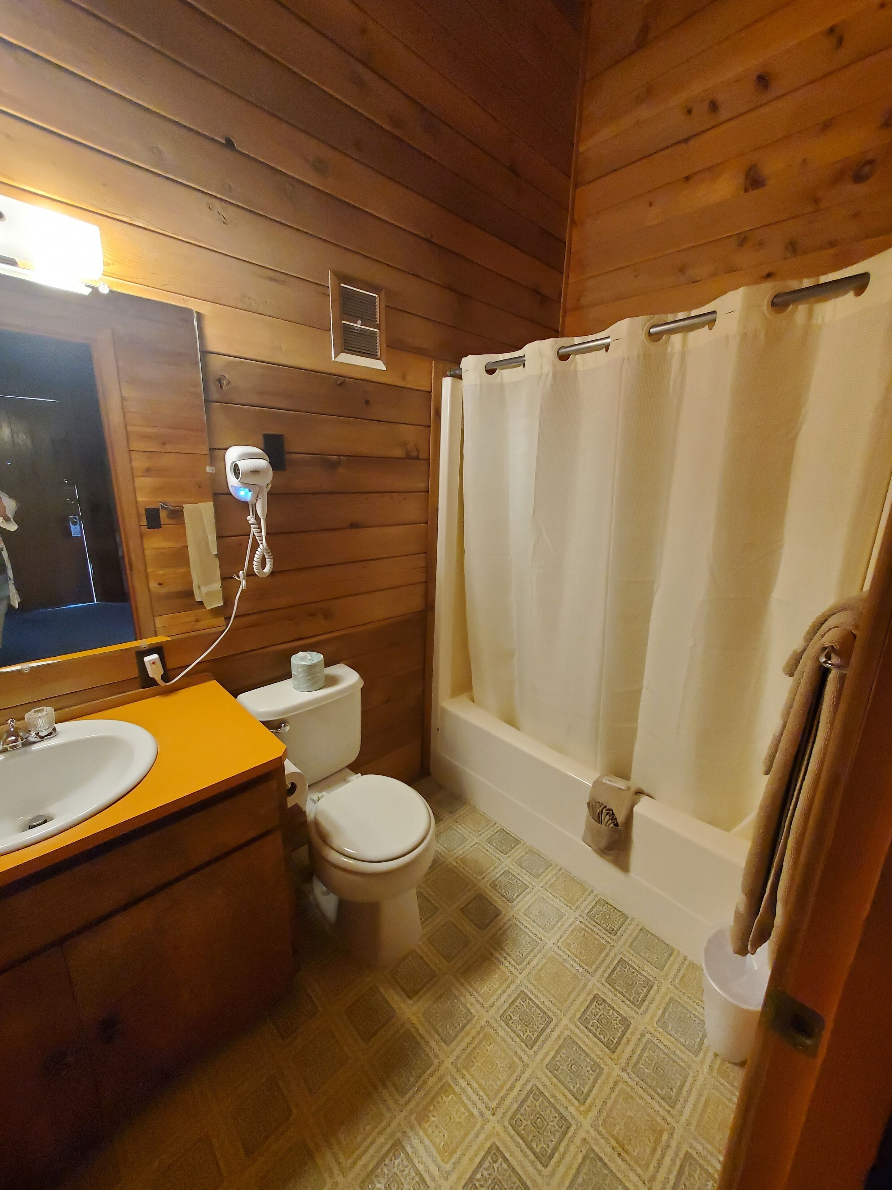 A wooden-paneled bathroom with a toilet, sink, and bathtub.
