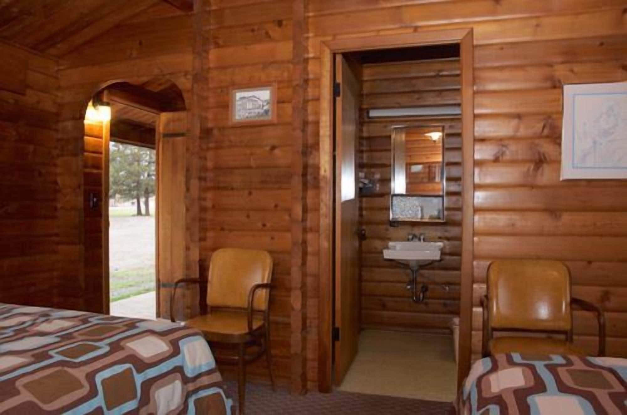A log cabin room with two beds, a sink, and a mirror.