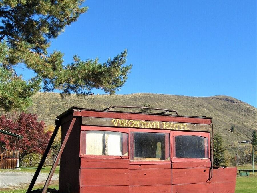 A red wooden carriage with the sign "VIRGINIATY HOTEL" on top, featuring large wooden wheels and a simple, rustic design.