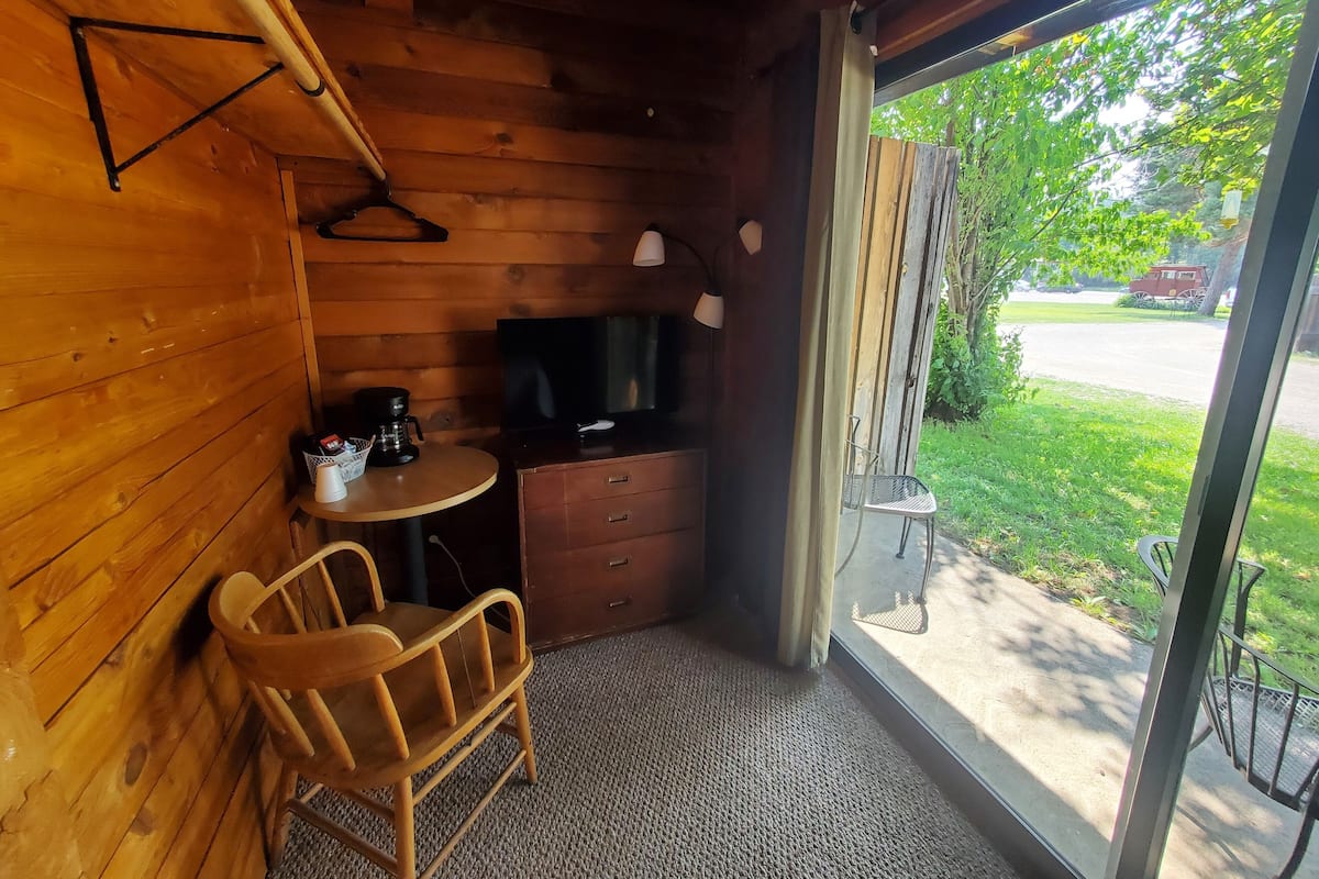 Una habitación acogedora con paredes de madera, una pequeña mesa redonda, una silla de madera, un televisor y vistas al exterior a través de un ventanal grande.
