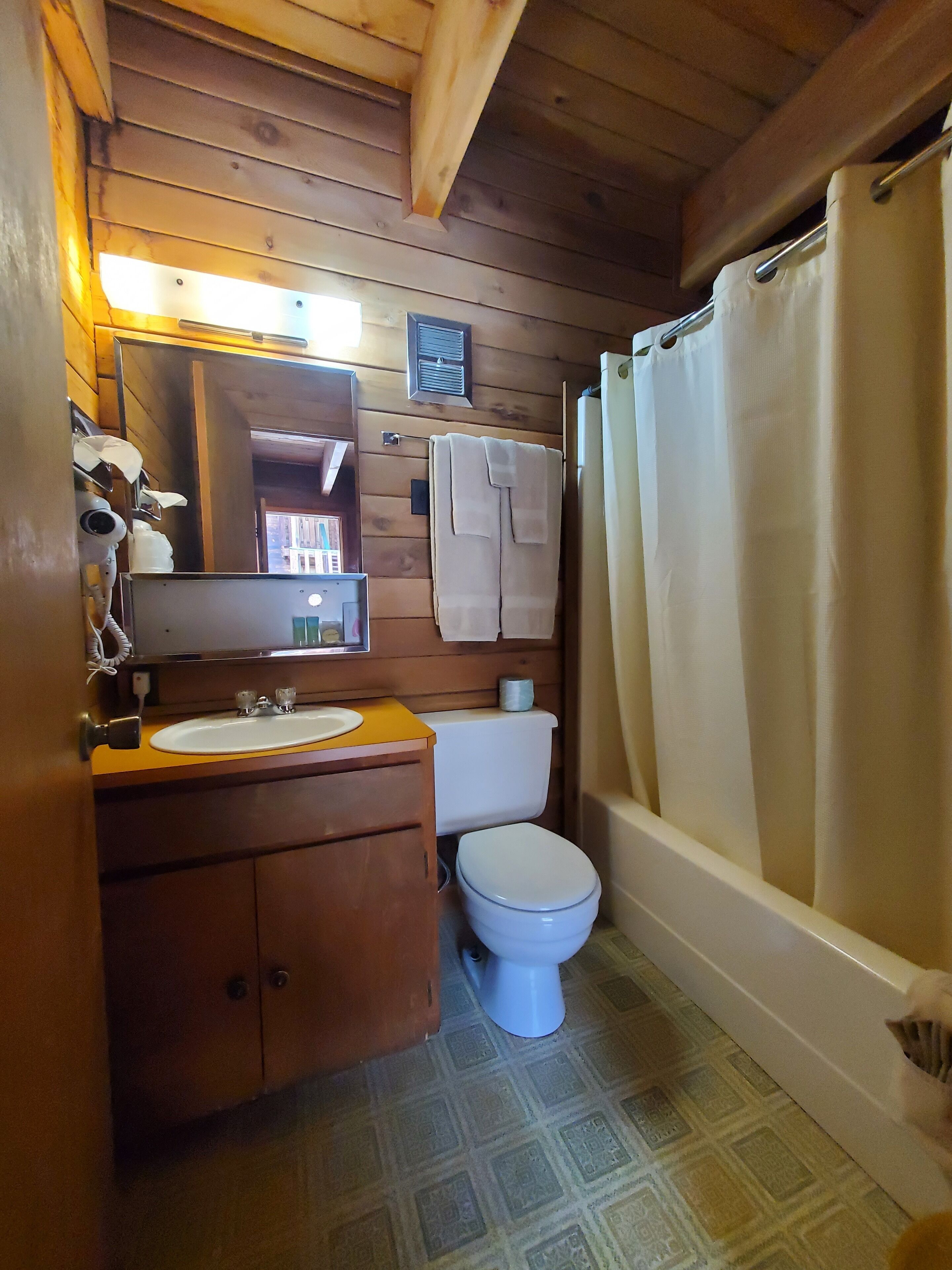 A wooden cabin bathroom with a sink, toilet, and shower curtain.