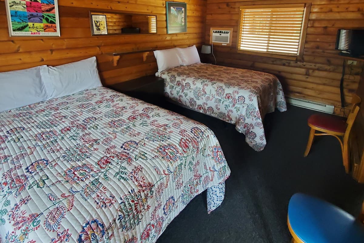 Una cabaña con dos camas, techo de madera y una pequeña mesa con una silla.