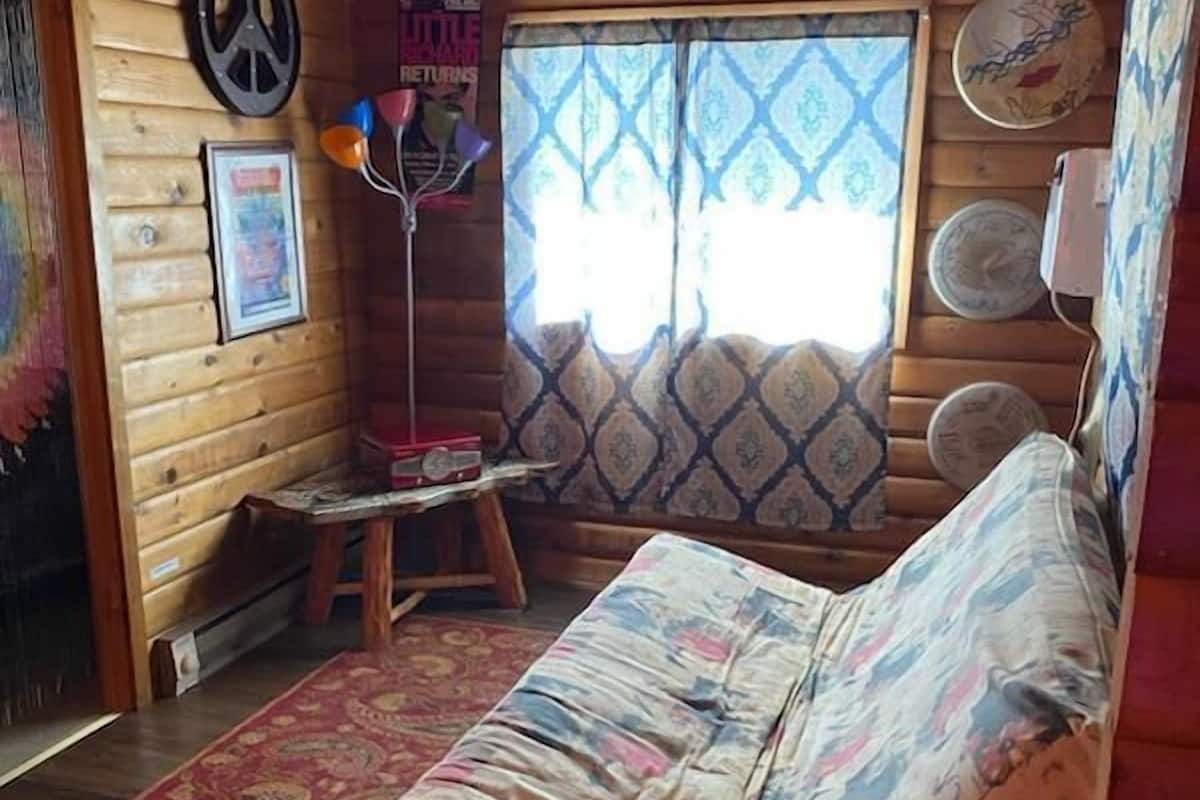 Una habitación acogedora de estilo cabaña, con paredes de madera, un banco acolchado, cortinas estampadas y un reloj decorativo en la pared.